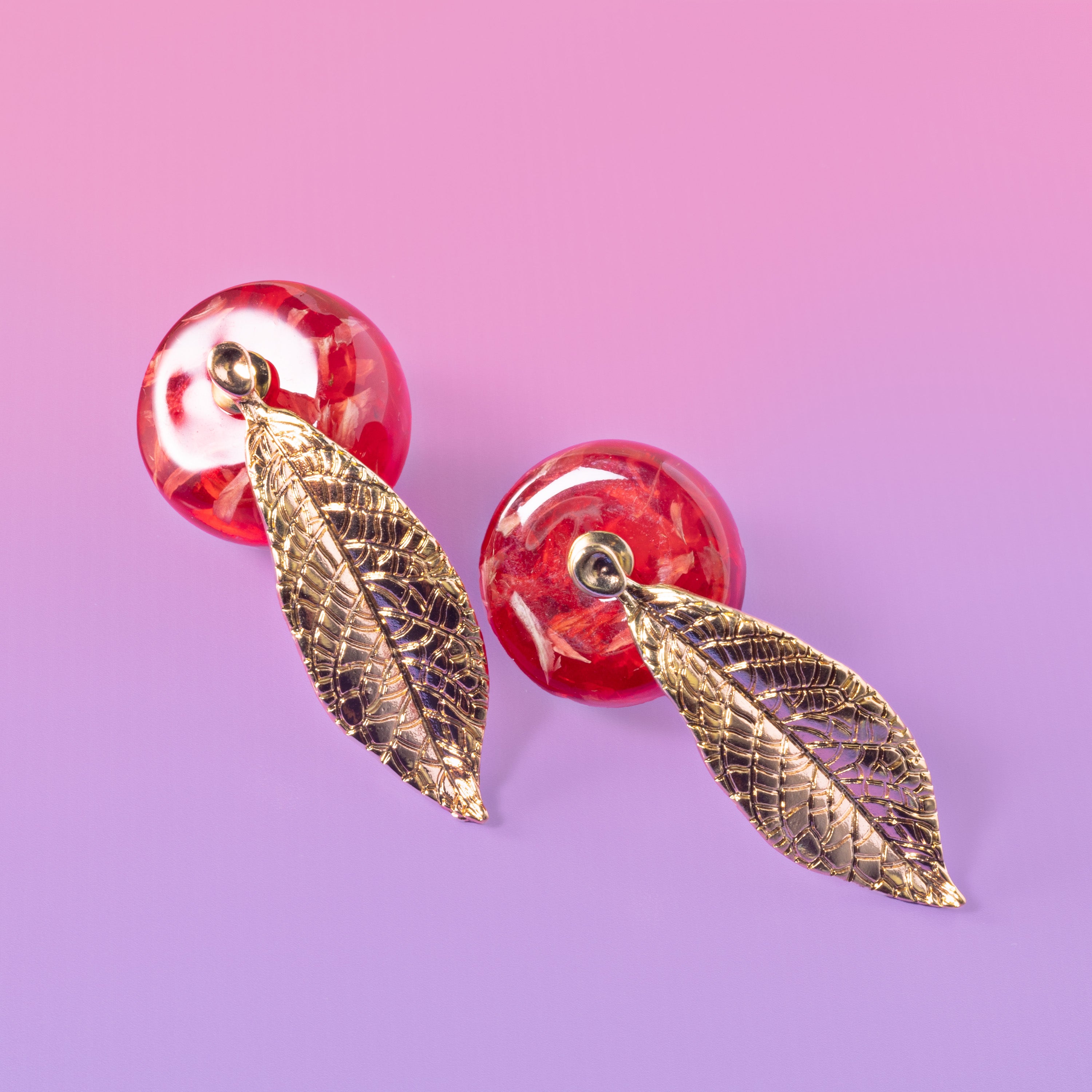 a pair of red and gold earrings on a purple background