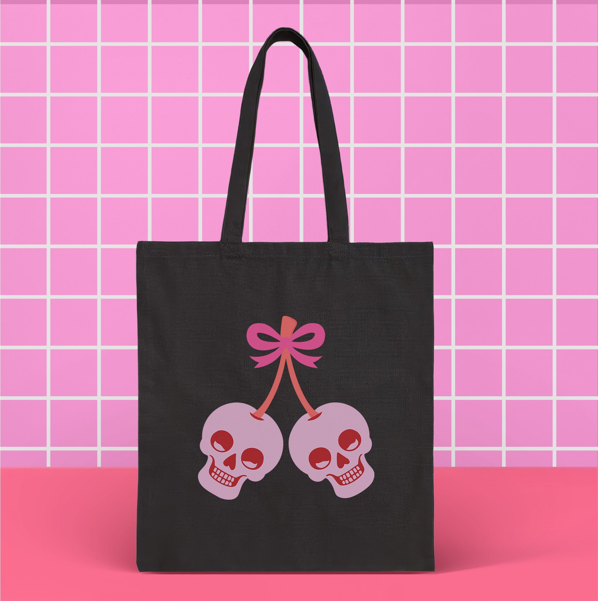 Canvas tote bag featuring pink skull cherries design. Two pink skulls connected by red stem and bow. Quirky gothic-inspired graphic on cream background. Stylish, edgy accessory for everyday use. Perfect for alternative fashion lovers.