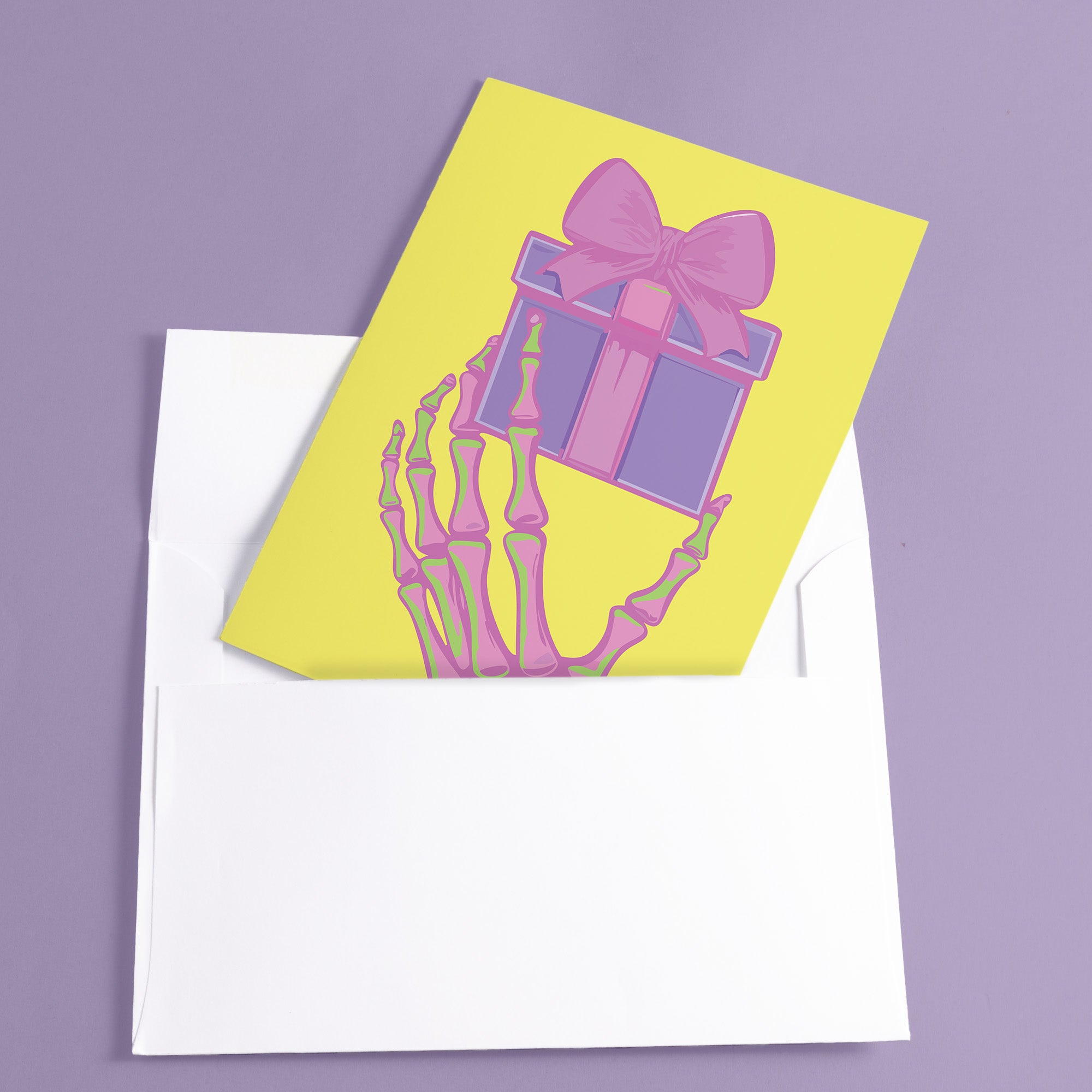 Birthday card with vibrant yellow background. A pink and green skeletal hand holds a purple and pink gift box with large pink bow. The illustration blends festive and spooky elements, creating a playful Halloween-meets-birthday aesthetic. The stylized, colorful design uses contrasting bright colors for a eye-catching effect. Inside message reads: 'Unwrap the Magic. Embrace the Spook. It's Your Day to Shine!' - combining celebratory spirit with a touch of the macabre for a unique birthday greeting.