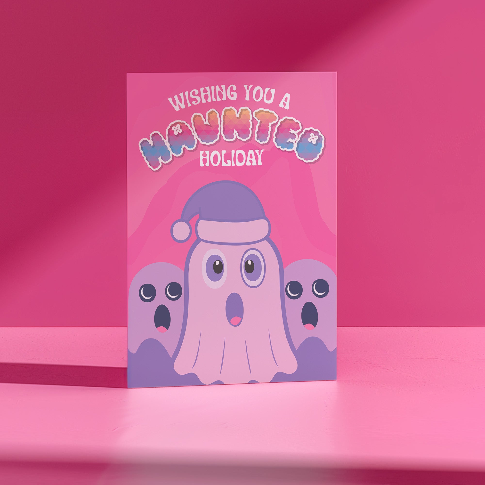 Holiday card with pink background featuring cartoon ghosts. Main ghost wears purple Santa hat. Text reads 