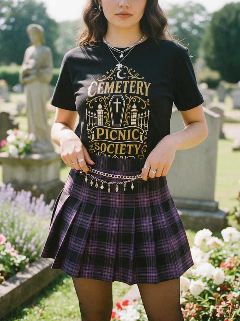 A black unisex crewneck graphic t-shirt featuring an ornate Victorian-inspired emblem printed on the chest in vintage gold and off-white. The centralized, symmetrical design showcases a classic coffin with a cross on the lid, flanked by wrought-iron cemetery gates. Beautiful scrollwork and decorative filigree flourishes surround the bold, retro serif text reading CEMETERY PICNIC SOCIETY. A crescent moon and stars sit at the top, completing this gothic memento mori graphic shirt.