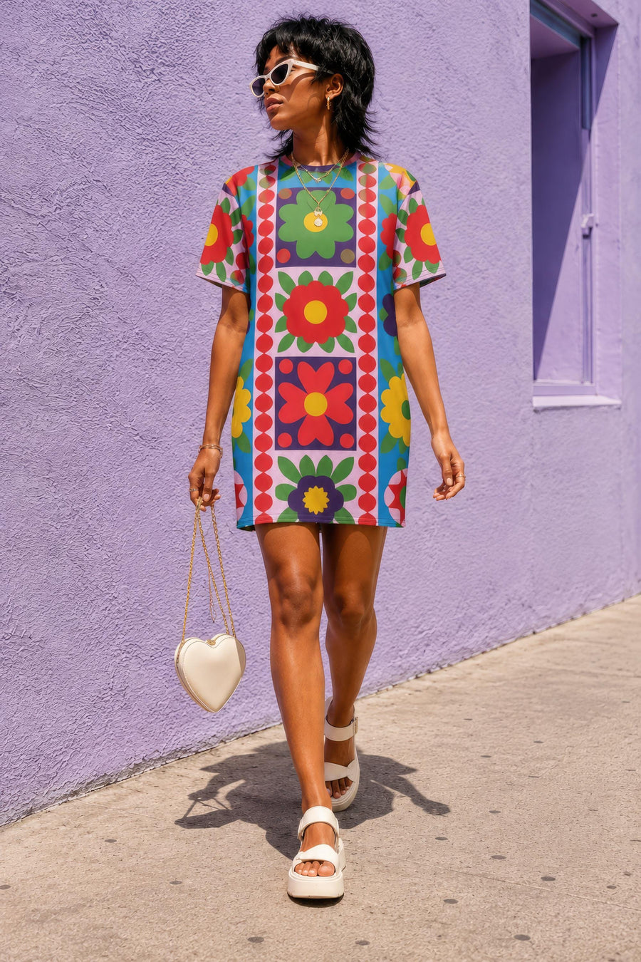 Short sleeve crew neck t-shirt dress in a relaxed, oversized straight cut, made of 100% polyester with a soft matte finish. An edge-to-edge all-over print shows 70s mod flowers in red, green, yellow, and purple set inside quilt-style patchwork panels of hot pink, royal blue, and lavender, divided by vertical stripes of red and pink polka dots. Retro 70s hippie, patchwork quilt, dopamine dressing maximalist alt fashion.