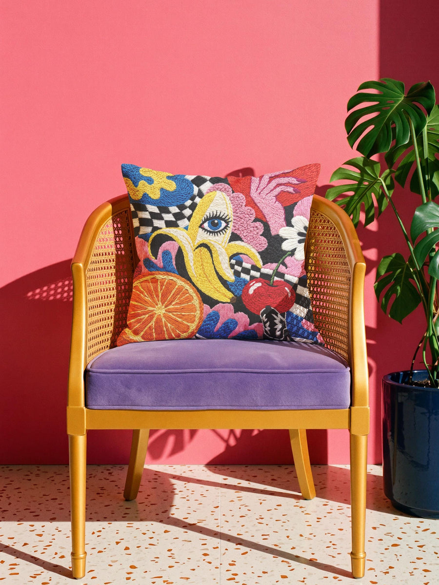 Square maximalist throw pillow cover with a surreal pop art fruit design printed to look like thick crewel embroidery on a dark background. A yellow banana peels open to reveal a large blue human eye, joined by an orange slice, a red cherry, pink manicured hands, a white daisy, and a winding black and white checkerboard ribbon. Smooth flat 2D print, not raised stitching. Eclectic, quirky dopamine decor for a sofa, accent chair, or breakfast nook.