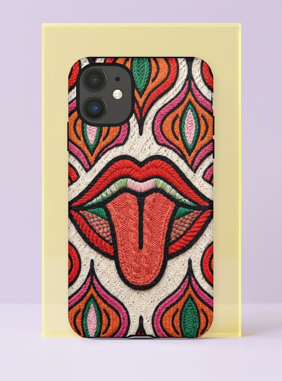 Dual layer matte phone case with a 2D print that mimics heavy crochet and thick knit yarn. A large open mouth with bright red lips and a red tongue sticking out sits at the center of a cream background, surrounded by mirrored teardrop and flame shapes in bright orange, dark green, and hot pink with black stitch-style outlines. Smooth printed surface with no raised threads, open ports, and camera cutout. Psychedelic 70s pop art phone accessory.